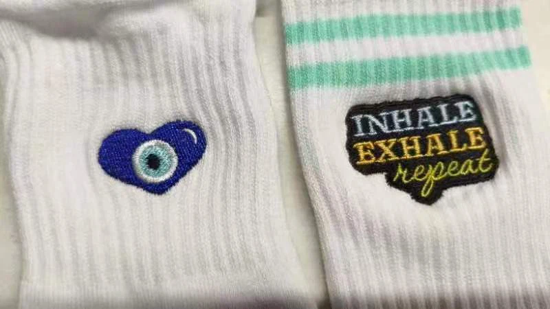 Close-up of custom embroidered socks with blue evil eye heart and INHALE EXHALE text embroidery
