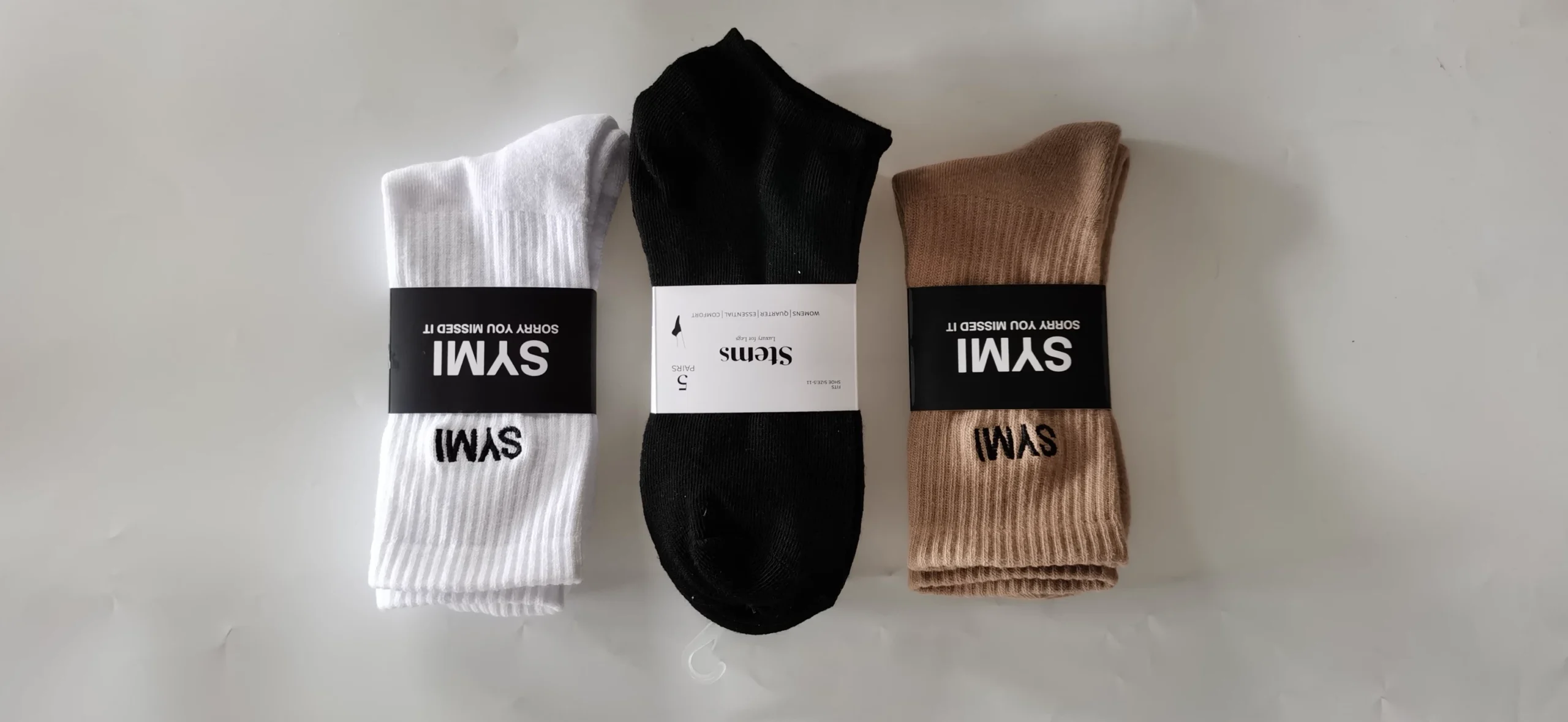 Three pairs of quarter socks in white black and tan with branded waistbands